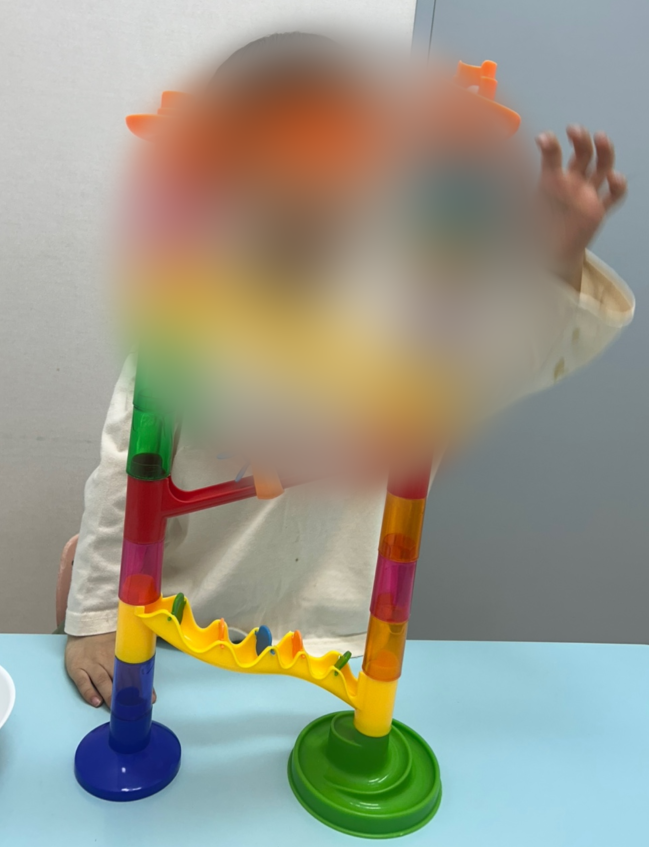 색색의 물레방아 장난감에 구슬을 굴리며 놀이하는 아이. 얼굴은 모자이크 처리됨